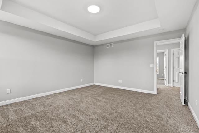 carpeted spare room featuring a tray ceiling, visible vents, and baseboards