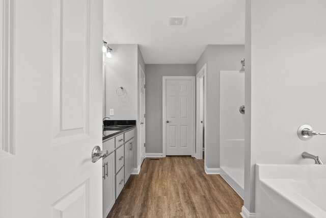 bathroom featuring visible vents, vanity, wood finished floors, baseboards, and a bath