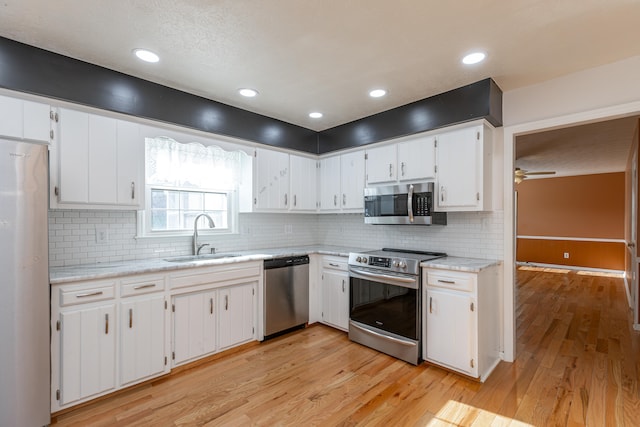 kitchen with sink, white cabinetry, light hardwood / wood-style floors, stainless steel appliances, and decorative backsplash