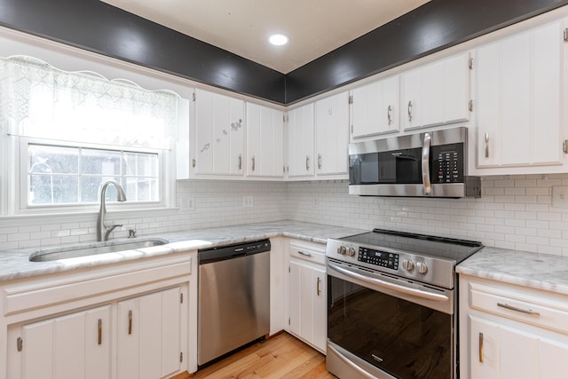 kitchen featuring white cabinets, backsplash, light wood-type flooring, sink, and stainless steel appliances