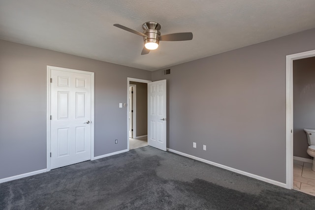 unfurnished bedroom featuring connected bathroom, ceiling fan, a textured ceiling, and dark carpet