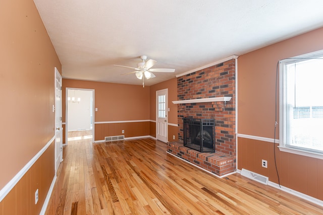 unfurnished living room featuring a brick fireplace, a textured ceiling, light wood-type flooring, and ceiling fan