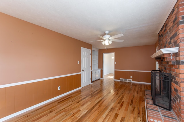 unfurnished living room with light hardwood / wood-style flooring, a textured ceiling, ceiling fan, and a brick fireplace