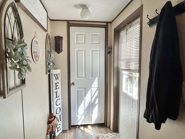 entryway with a textured ceiling, ornamental molding, and light hardwood / wood-style flooring