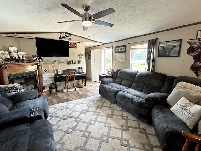 living room featuring ceiling fan, hardwood / wood-style floors, lofted ceiling, ornamental molding, and a textured ceiling