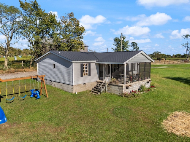 rear view of property featuring a sunroom, a yard, and a playground