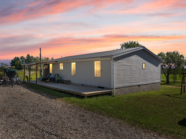 back house at dusk featuring a wooden deck and a lawn