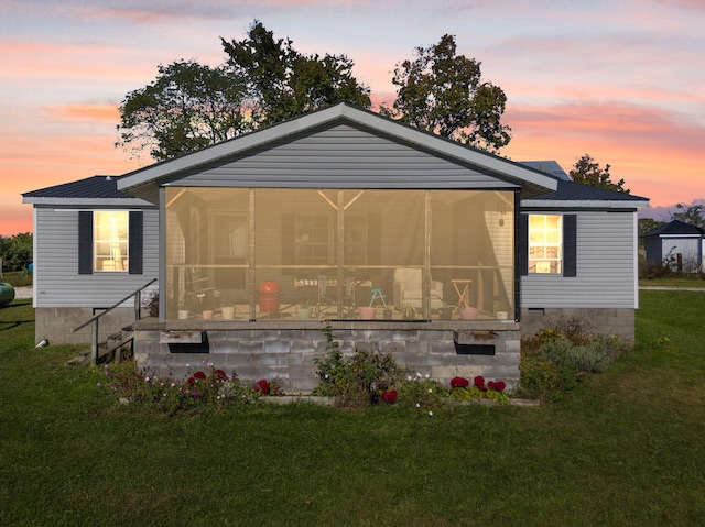 back house at dusk featuring a sunroom and a lawn