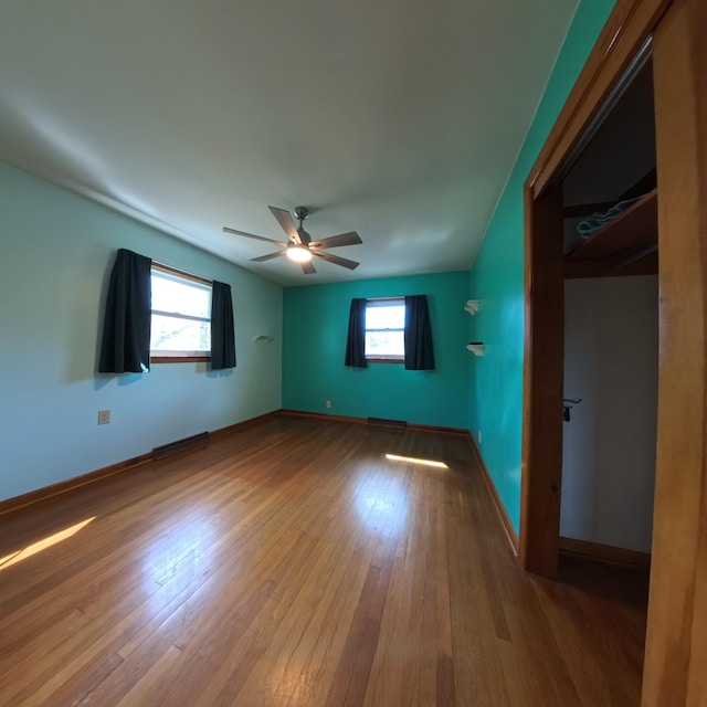 unfurnished bedroom featuring ceiling fan, multiple windows, wood finished floors, and baseboards