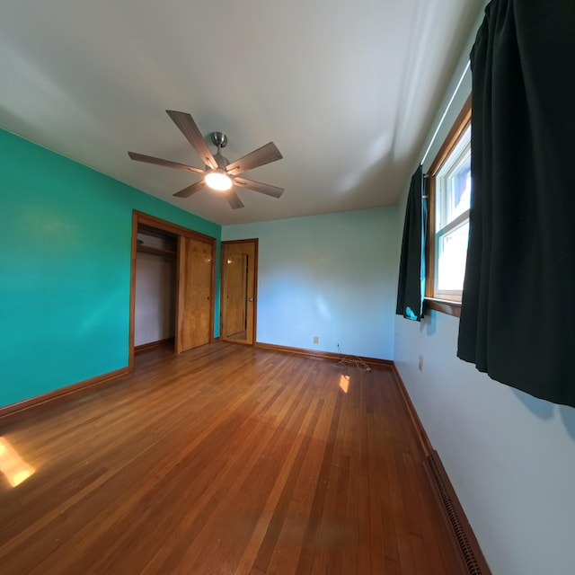 unfurnished bedroom with wood finished floors, a ceiling fan, visible vents, baseboards, and a closet