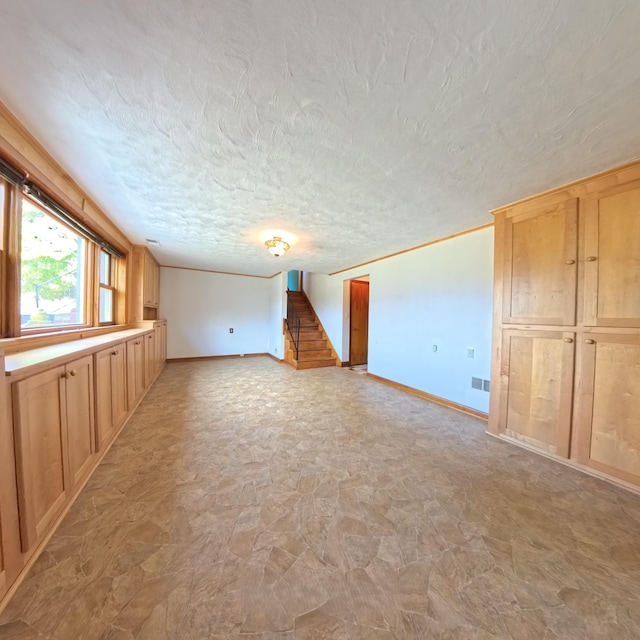 unfurnished living room featuring a textured ceiling, visible vents, baseboards, stairs, and ornamental molding