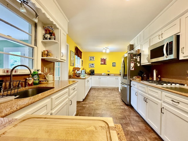 kitchen with light stone counters, open shelves, stainless steel appliances, white cabinetry, and a sink