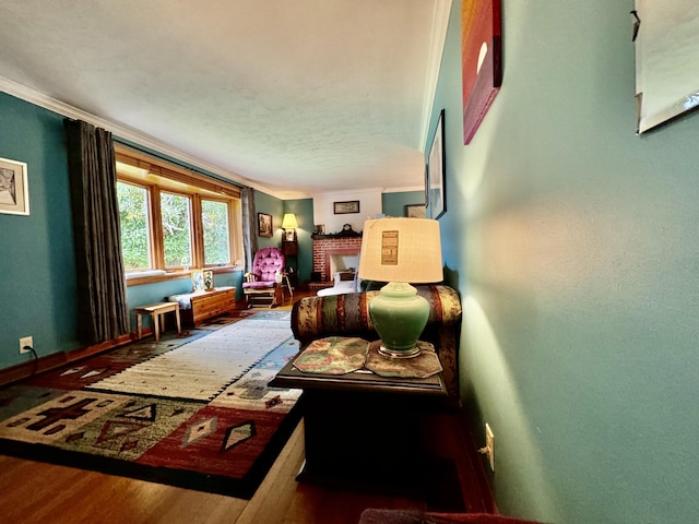 sitting room featuring a brick fireplace, baseboards, wood finished floors, and ornamental molding