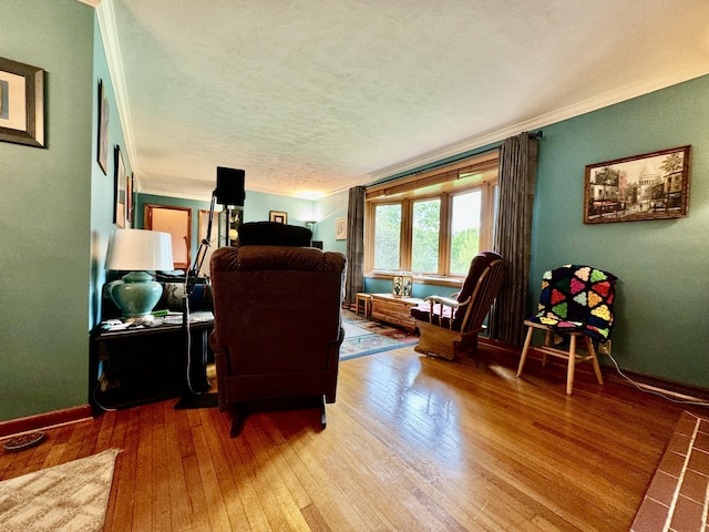 living area with a textured ceiling, ornamental molding, wood finished floors, and baseboards