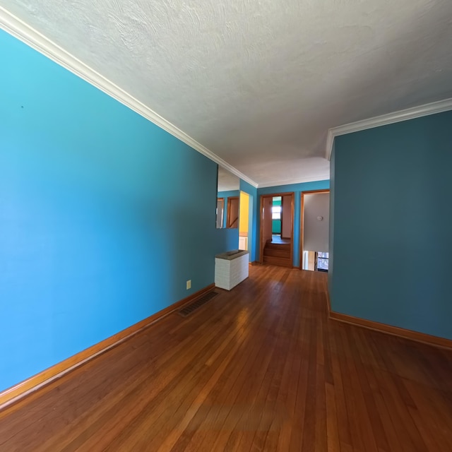 empty room featuring a textured ceiling, wood finished floors, visible vents, baseboards, and ornamental molding