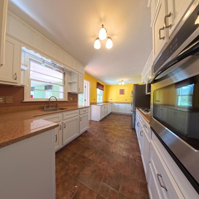 kitchen featuring light stone counters, open shelves, stainless steel appliances, white cabinetry, and a sink