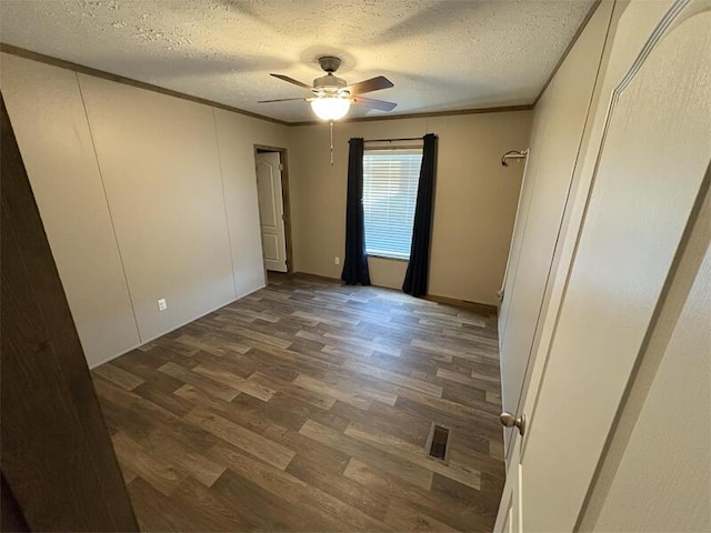 unfurnished room featuring ceiling fan, dark wood-type flooring, a textured ceiling, and ornamental molding