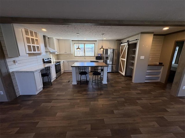 kitchen with appliances with stainless steel finishes, wall chimney range hood, a barn door, white cabinets, and a kitchen island