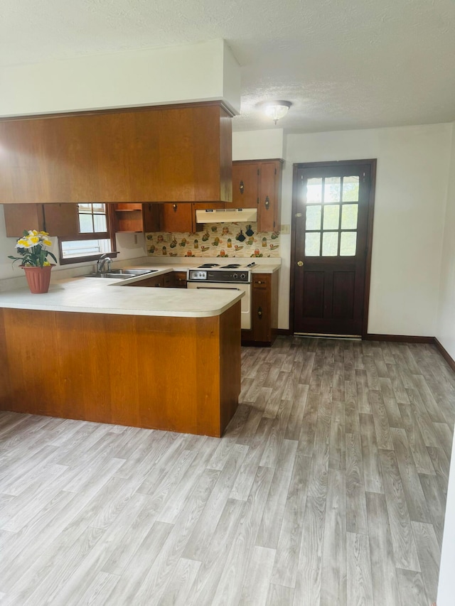 kitchen featuring light wood-type flooring, sink, kitchen peninsula, white range, and decorative backsplash