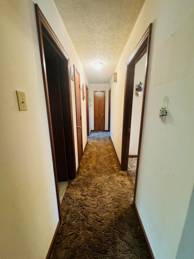 hall with a textured ceiling and dark carpet