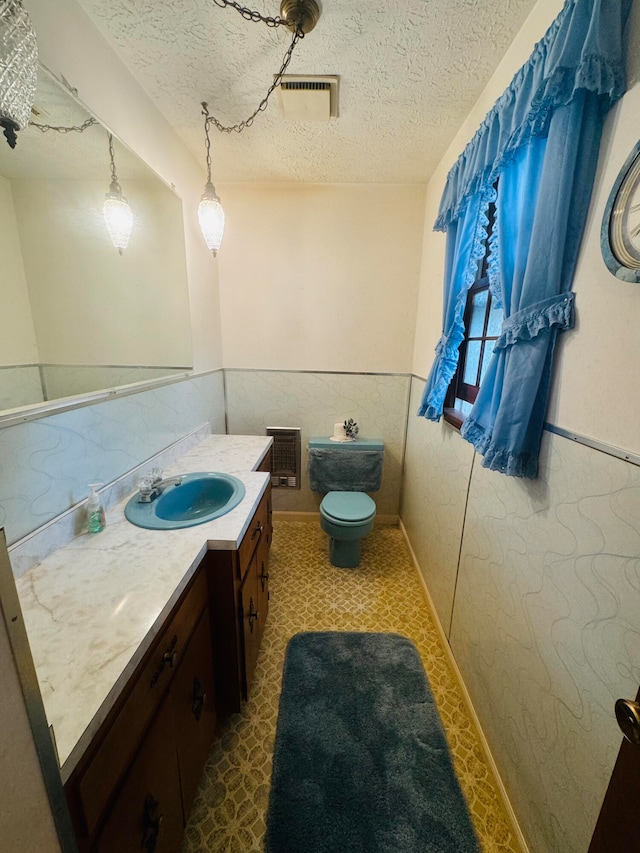 bathroom featuring heating unit, a textured ceiling, vanity, and toilet