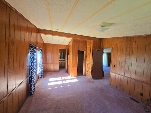 unfurnished room with beam ceiling, wood walls, and carpet floors