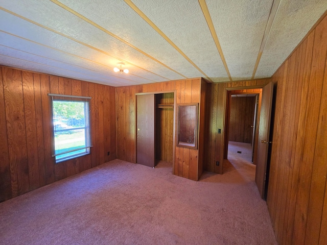 unfurnished bedroom featuring a textured ceiling, carpet flooring, wooden walls, and a closet