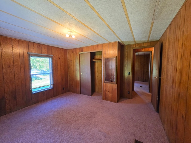 unfurnished bedroom with wooden walls, a closet, carpet flooring, and a textured ceiling