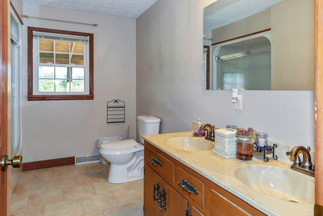 bathroom featuring a textured ceiling, vanity, toilet, and a shower with shower door