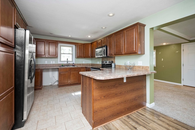 kitchen featuring sink, kitchen peninsula, appliances with stainless steel finishes, a breakfast bar, and light carpet