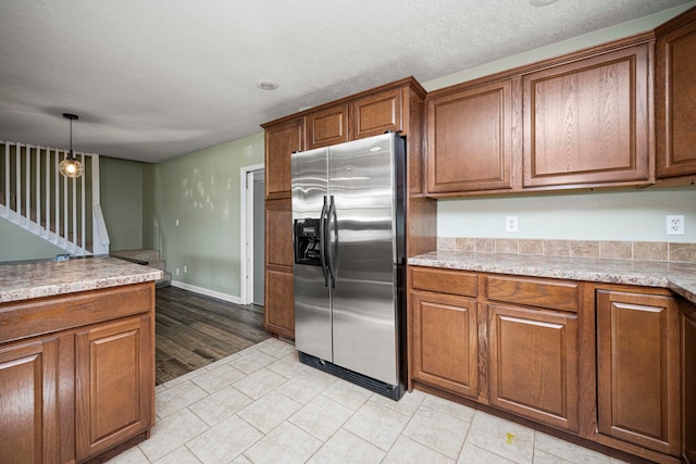 kitchen with pendant lighting, a textured ceiling, stainless steel refrigerator with ice dispenser, light stone countertops, and light hardwood / wood-style floors