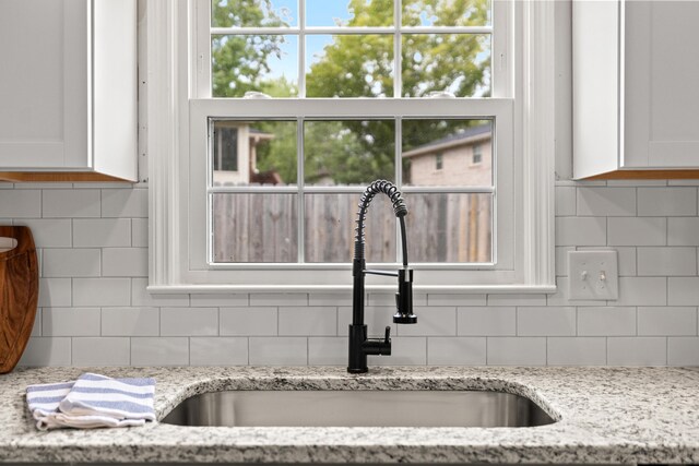 details with backsplash, light stone countertops, and sink