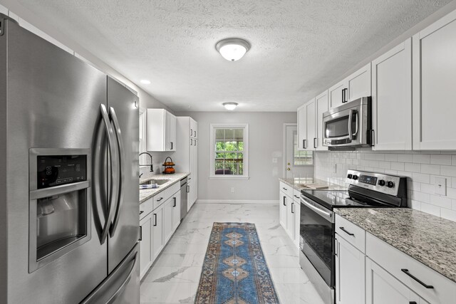 kitchen featuring sink, white cabinetry, appliances with stainless steel finishes, light stone countertops, and decorative backsplash