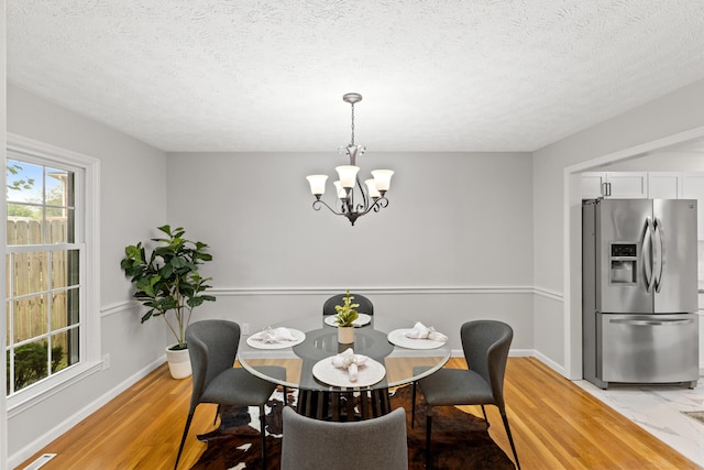 dining space featuring light hardwood / wood-style flooring, a textured ceiling, and a notable chandelier