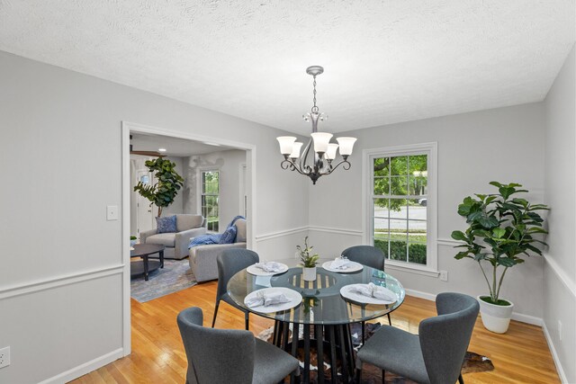 dining area with a textured ceiling, light wood-type flooring, and a notable chandelier