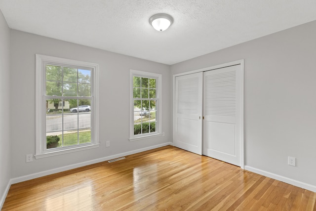 unfurnished bedroom with light wood-type flooring, a textured ceiling, and a closet