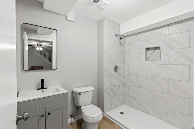 bathroom with vanity, a tile shower, toilet, ceiling fan, and hardwood / wood-style floors