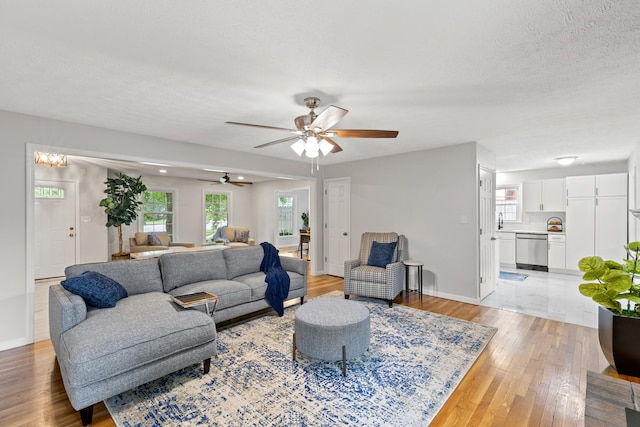 living room with a textured ceiling, ceiling fan, and light hardwood / wood-style flooring