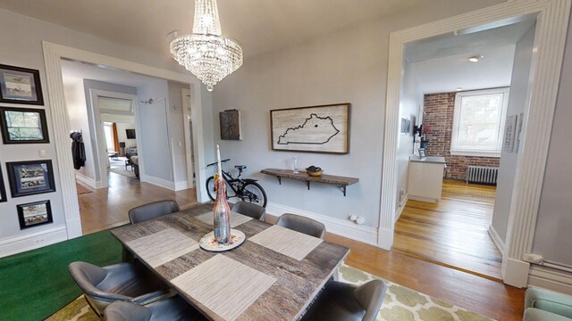 dining area featuring radiator, light hardwood / wood-style floors, and brick wall