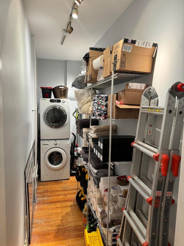 laundry room featuring track lighting, stacked washer / drying machine, and hardwood / wood-style floors