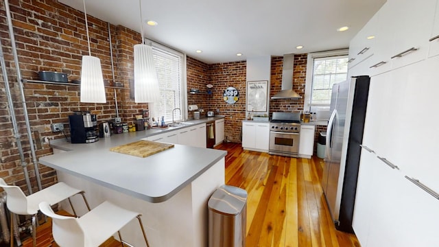 kitchen featuring appliances with stainless steel finishes, light hardwood / wood-style floors, brick wall, wall chimney exhaust hood, and kitchen peninsula