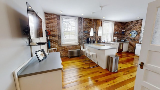 kitchen featuring pendant lighting, white cabinets, radiator heating unit, brick wall, and light hardwood / wood-style floors