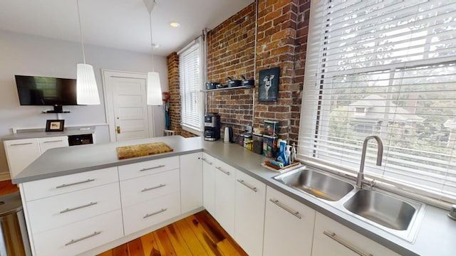 kitchen with hanging light fixtures, white cabinetry, kitchen peninsula, hardwood / wood-style flooring, and sink