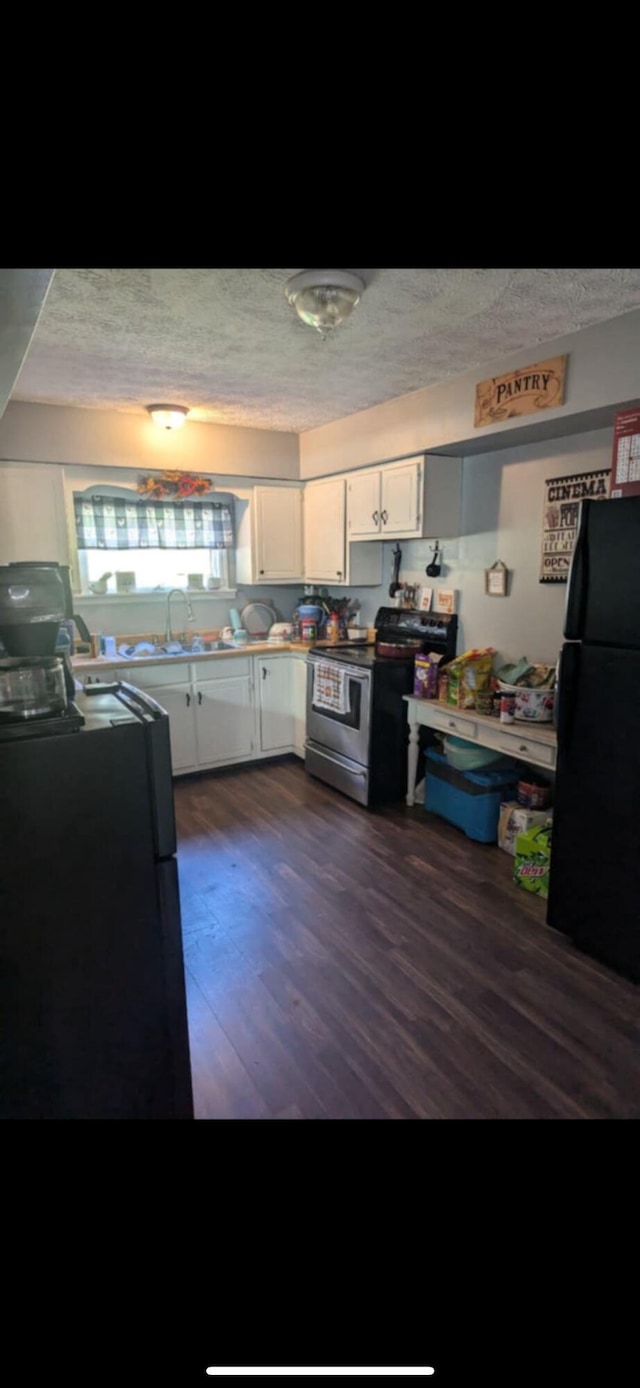 kitchen featuring stainless steel range with electric stovetop, a textured ceiling, black refrigerator, white cabinets, and dark wood-type flooring