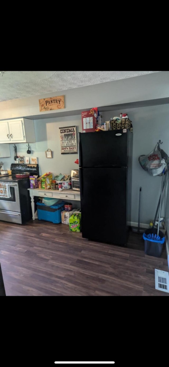 kitchen with black fridge, dark wood-type flooring, white cabinets, a textured ceiling, and stainless steel range oven