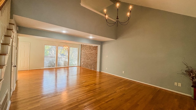 spare room with an inviting chandelier, light wood-type flooring, and high vaulted ceiling