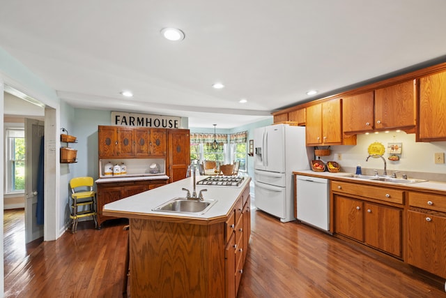 kitchen with dark hardwood / wood-style floors, a center island with sink, sink, decorative light fixtures, and white appliances