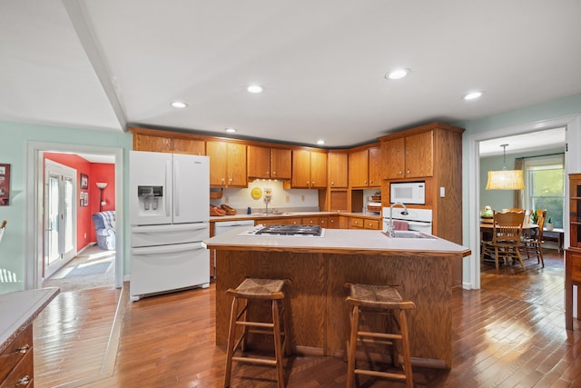 kitchen with an island with sink, wood-type flooring, sink, decorative light fixtures, and white appliances