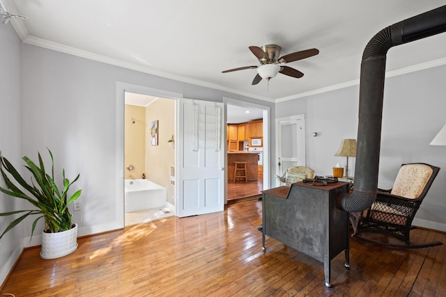 sitting room with ceiling fan, crown molding, a wood stove, and hardwood / wood-style floors