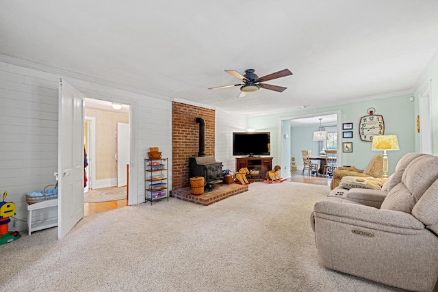 carpeted living room with ornamental molding, a wood stove, and ceiling fan